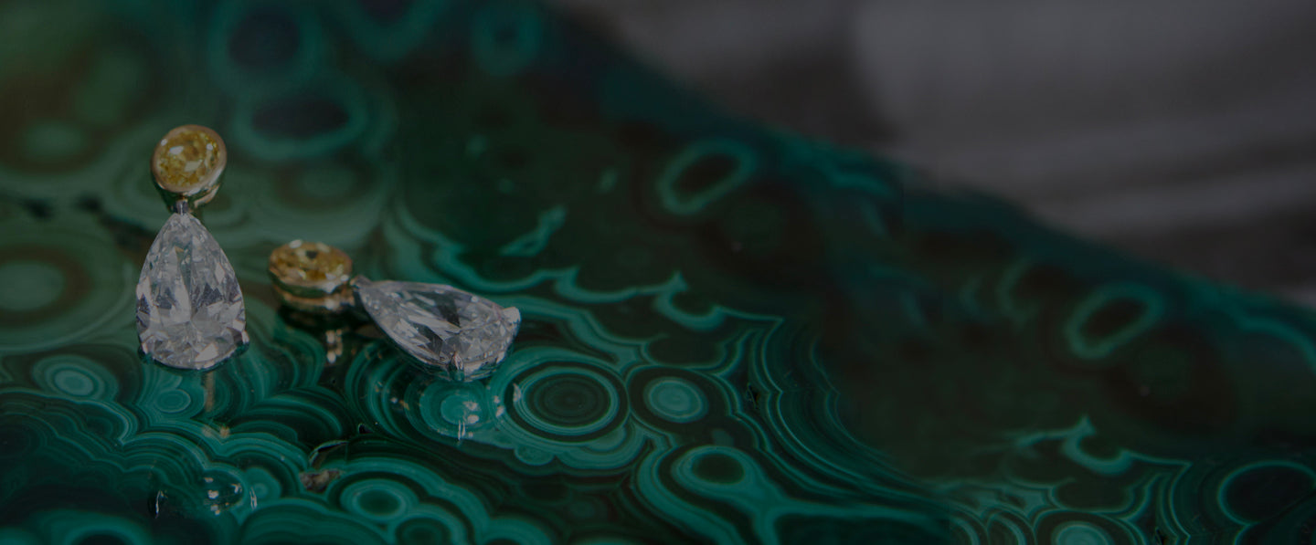 Two pairs of diamond and yellow gemstone earrings rest on a swirling green and black malachite surface.