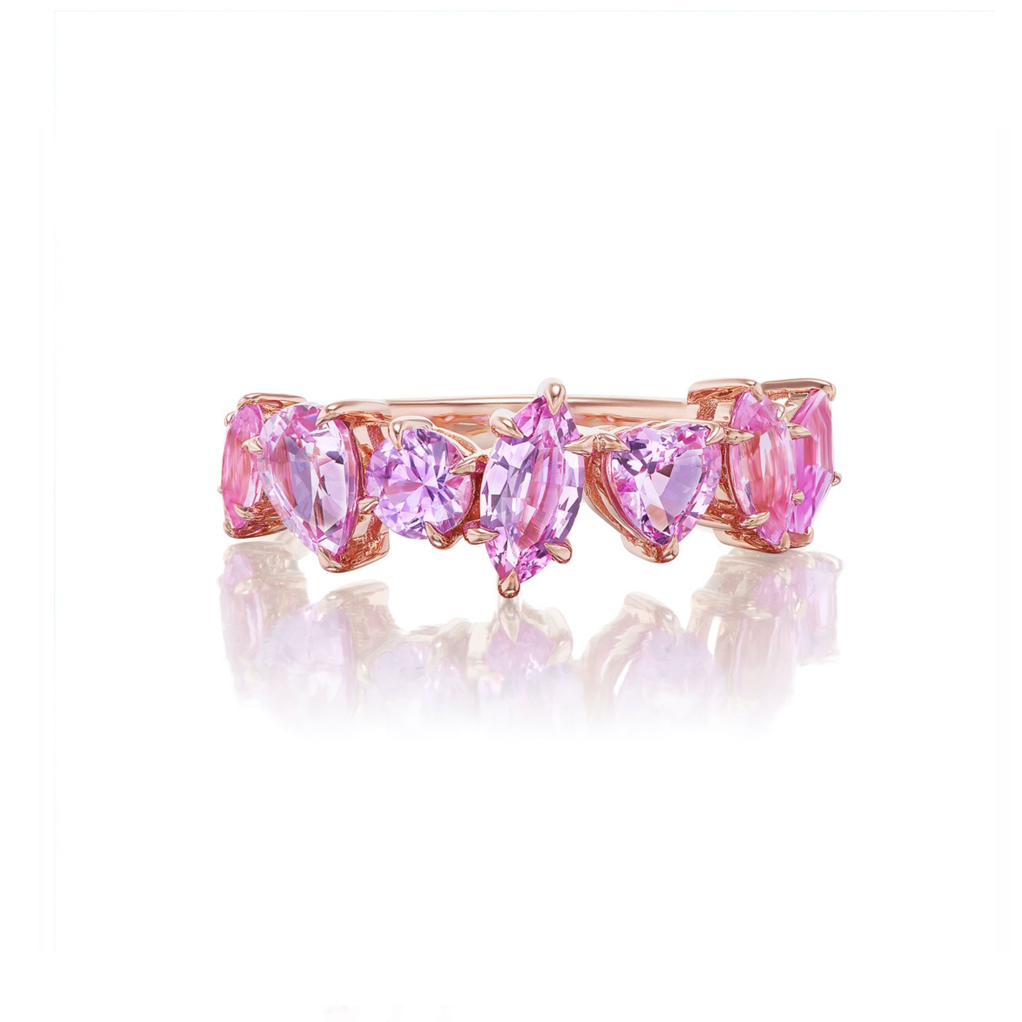 A gold ring set with oval, heart, and marquise-cut pink and lavender gemstones, arranged in a sparkling row, displayed on a white reflective surface.