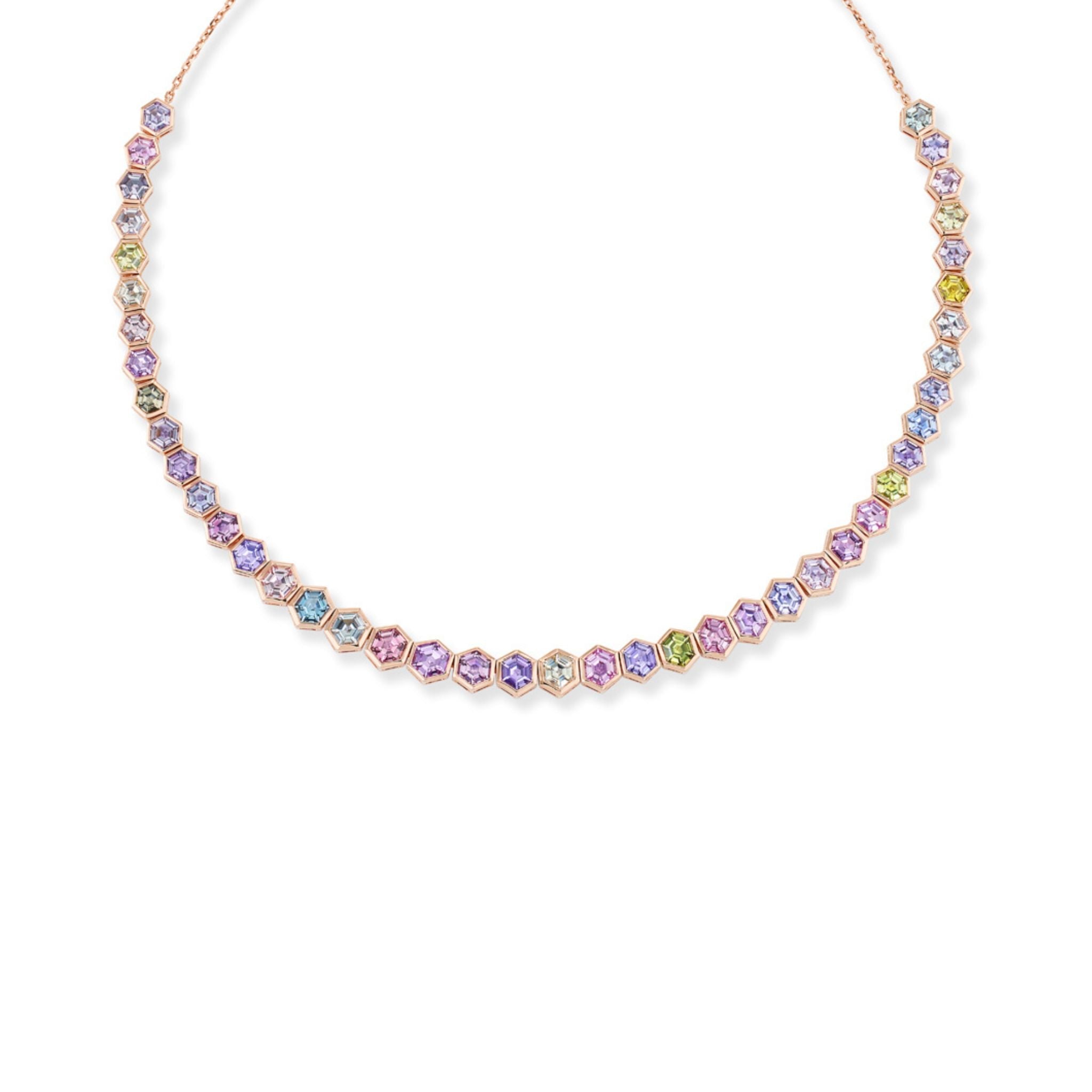 A gold necklace with hexagonal pastel gemstones in pink, purple, blue, and green, evenly spaced around the chain, displayed on a white background.