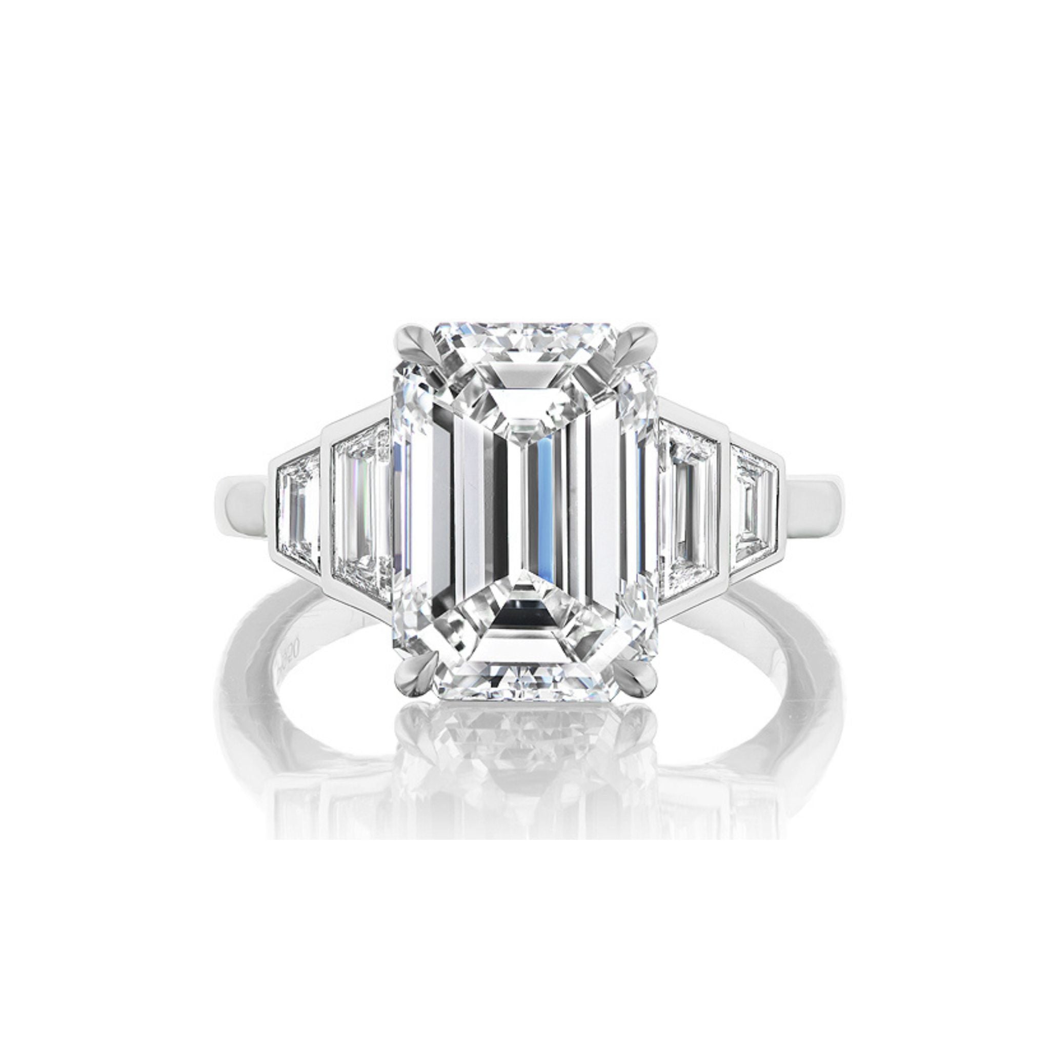 A platinum ring featuring a large emerald-cut diamond at the center, flanked by two trapezoid-shaped side diamonds and two smaller triangular diamonds, displayed on a white background.