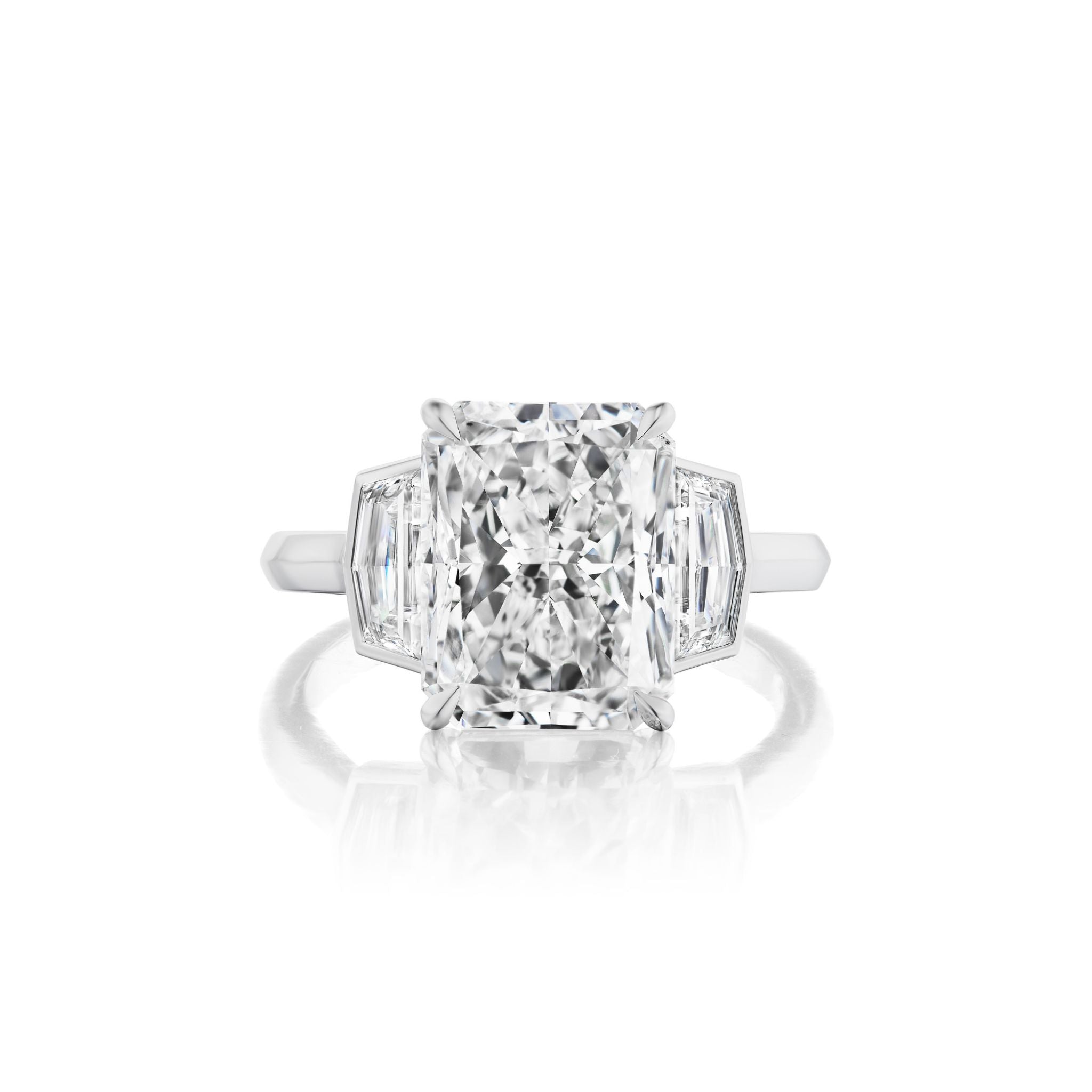 A radiant-cut diamond ring with two trapezoid side diamonds set in a white metal band, shown on a white background.