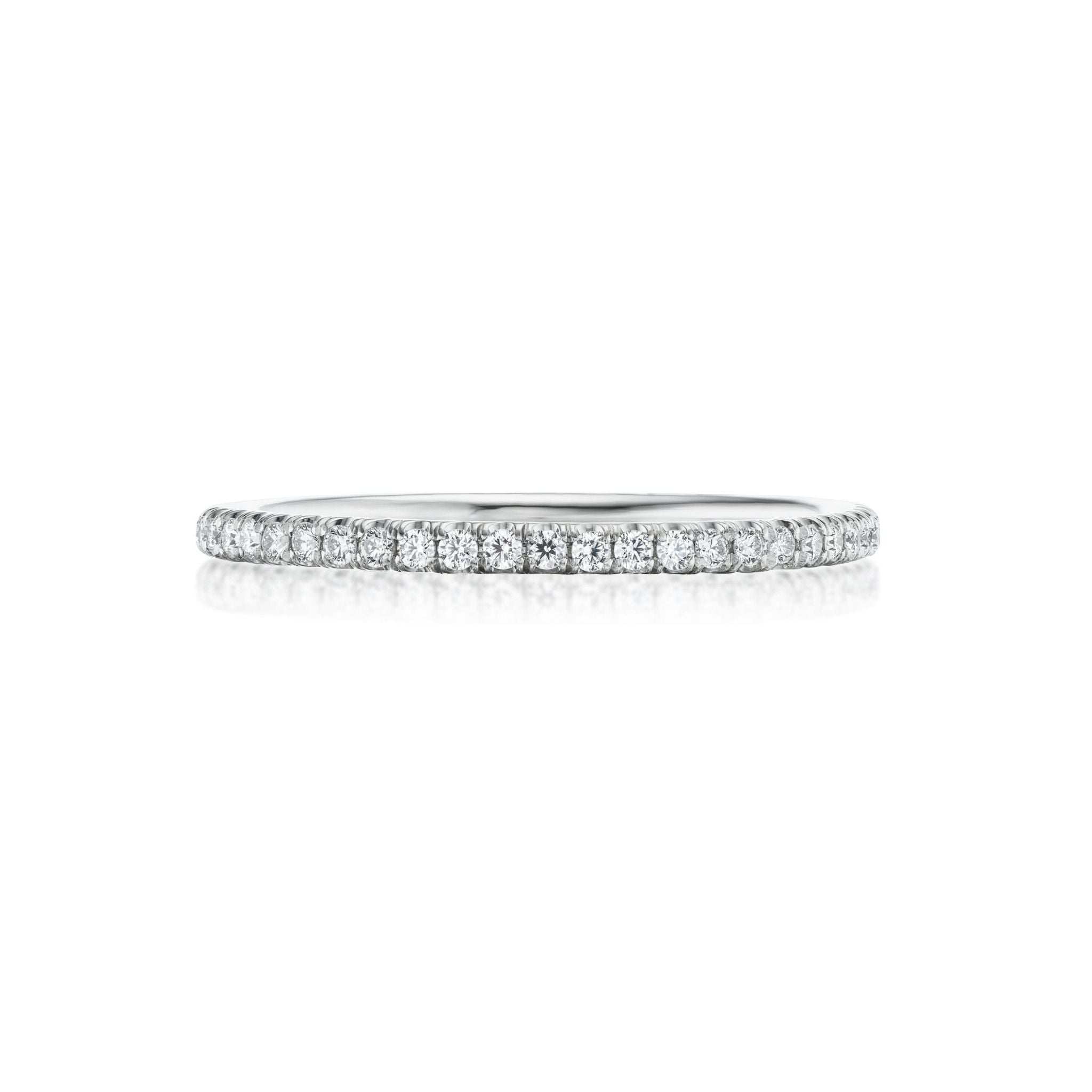 A thin, white gold or platinum ring featuring a continuous row of small, round diamonds set along the band, displayed on a white background with a subtle reflection below.