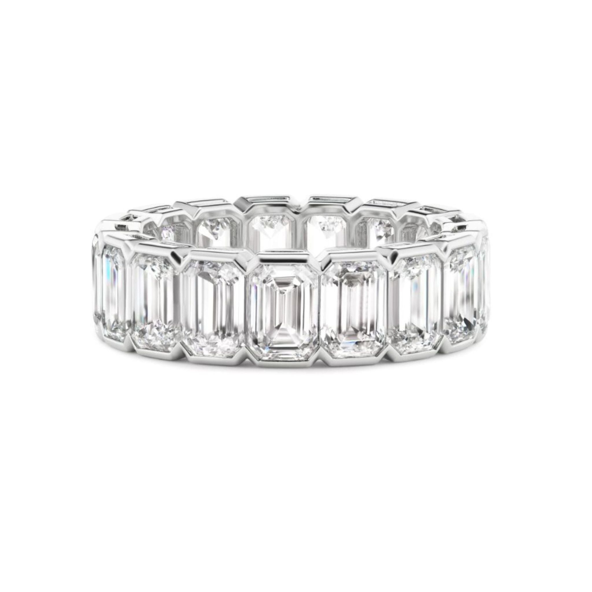 A white gold or platinum ring featuring a row of rectangular emerald-cut diamonds set closely together, displayed on a white background with a slight reflection beneath it.