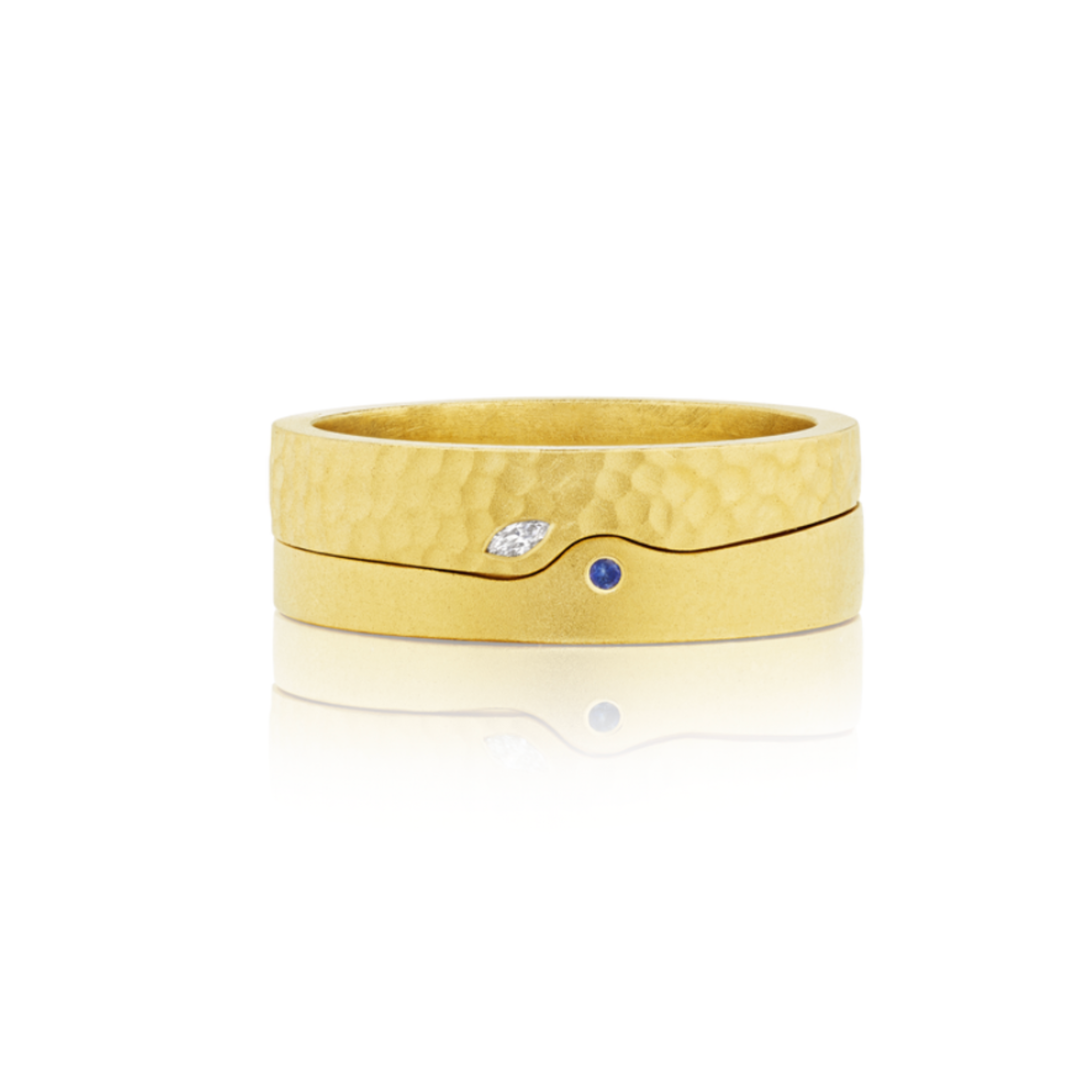 A pair of matching gold rings with a hammered texture; one features a small marquise diamond, and the other a tiny round blue sapphire. Both are displayed on a white background.
