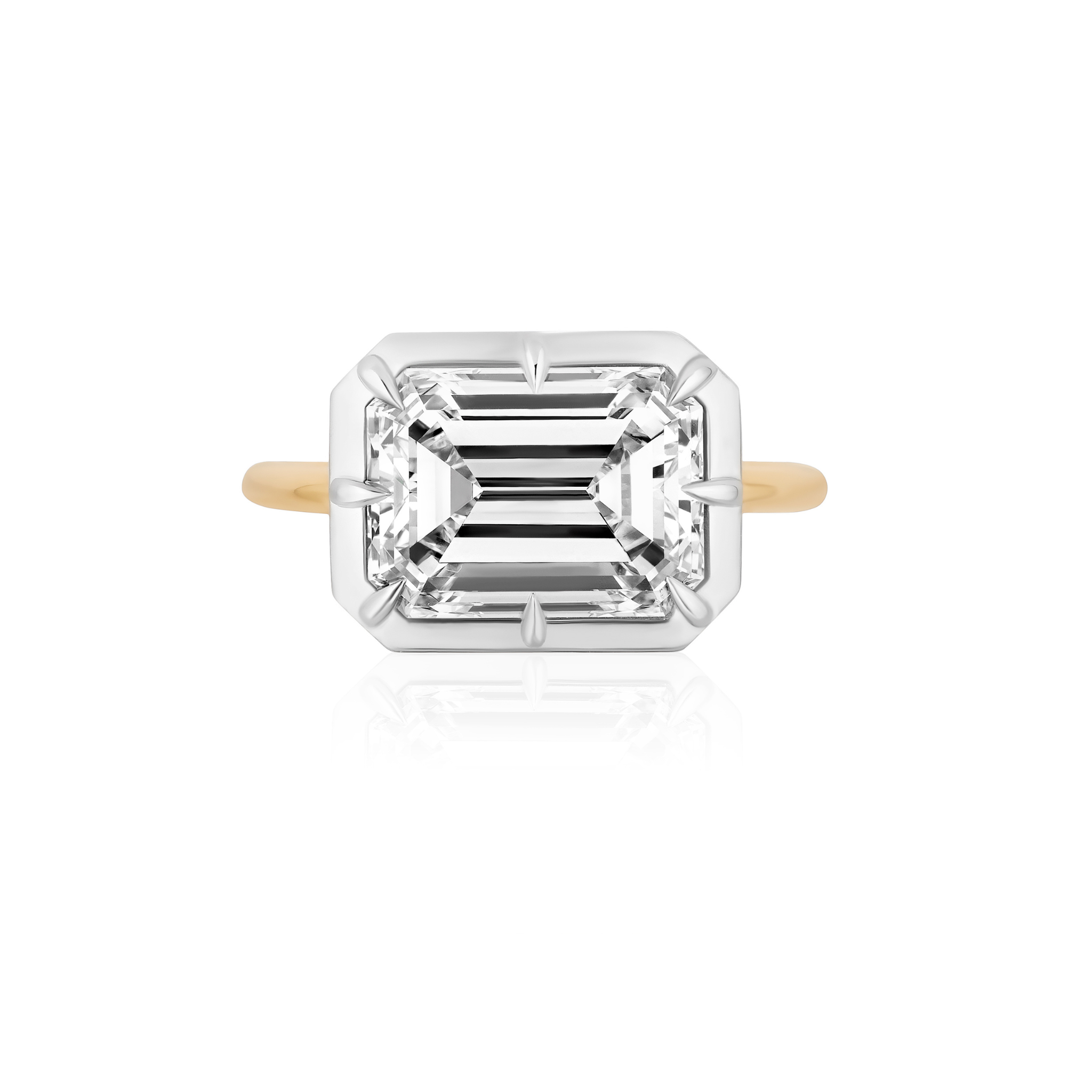 A gold ring with a large, rectangular emerald-cut diamond in a four-prong white metal setting, viewed from above on a white background.