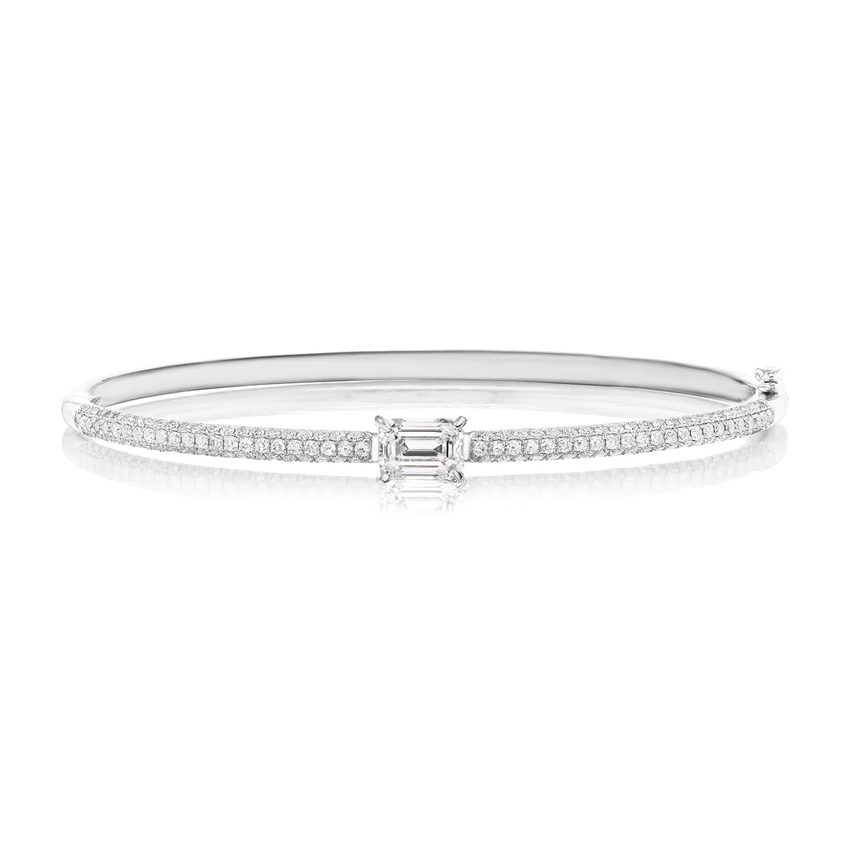 The East-West Emerald Cut Diamond Pavé Bangle showcases an emerald-cut diamond centerpiece between two smaller stones, set in 18K white gold and accented with pavé-set round diamonds along the band.