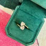 The Double Heart Wrap Around Ring, featuring 2.07tcw diamonds set in 18K yellow gold, is showcased in a green velvet box atop a vibrant, patterned surface.