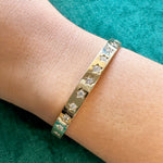 The Celestial Seeing Stars Diamond Bangle, crafted in 18k gold with star-shaped cutouts and sparkling diamonds, is elegantly displayed on a wrist against a teal fabric background.