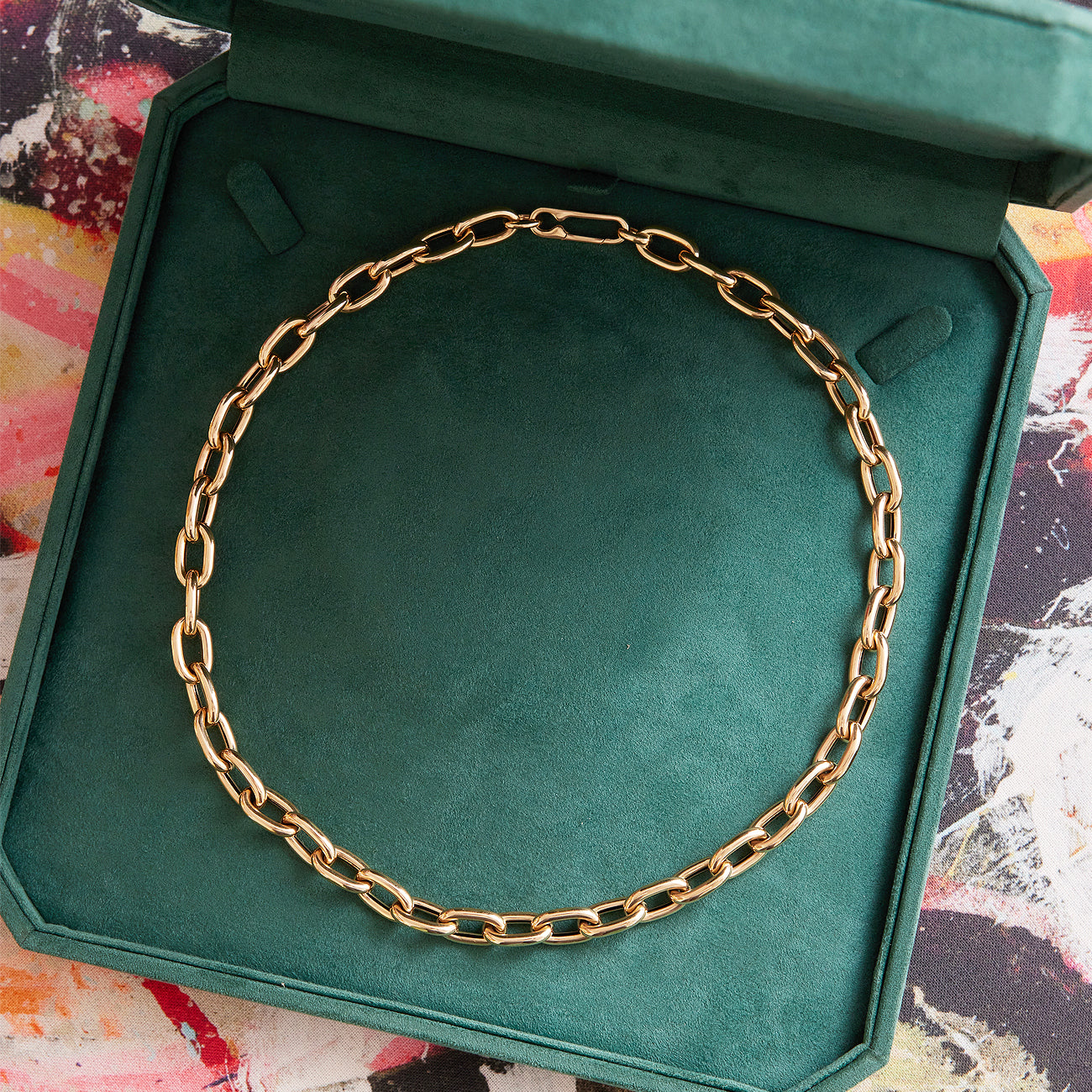 The Serpentine Signature Chain Necklace, an 18-inch customizable piece in 14K yellow gold, rests in an open green velvet jewelry box against a vibrant abstract backdrop.