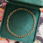 The Serpentine Signature Chain Necklace, an 18-inch customizable piece in 14K yellow gold, rests in an open green velvet jewelry box against a vibrant abstract backdrop.