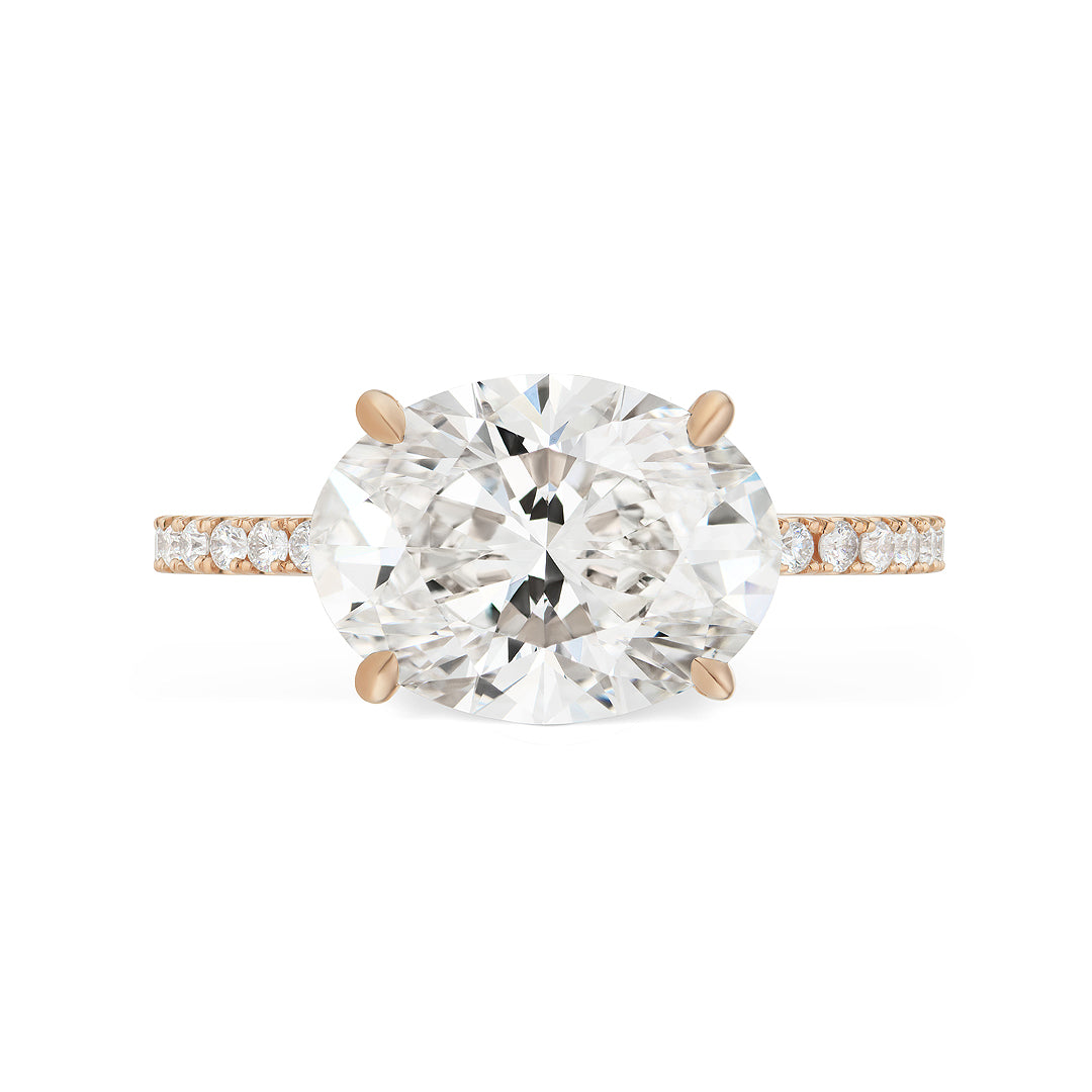 The East-West Oval Diamond Engagement Ring with Pavé Band features an oval-cut center diamond set in four prongs on a gold band with pavé-set round diamonds. This stunning bridal ring is shown against a plain white background.