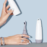 A hand opens a white case to reveal a gray tool from the Juli Diamond Cleaning Essentials Kit. Another hand with light blue nails and silver rings rests on a light blue surface, while a second closed case stands upright nearby.