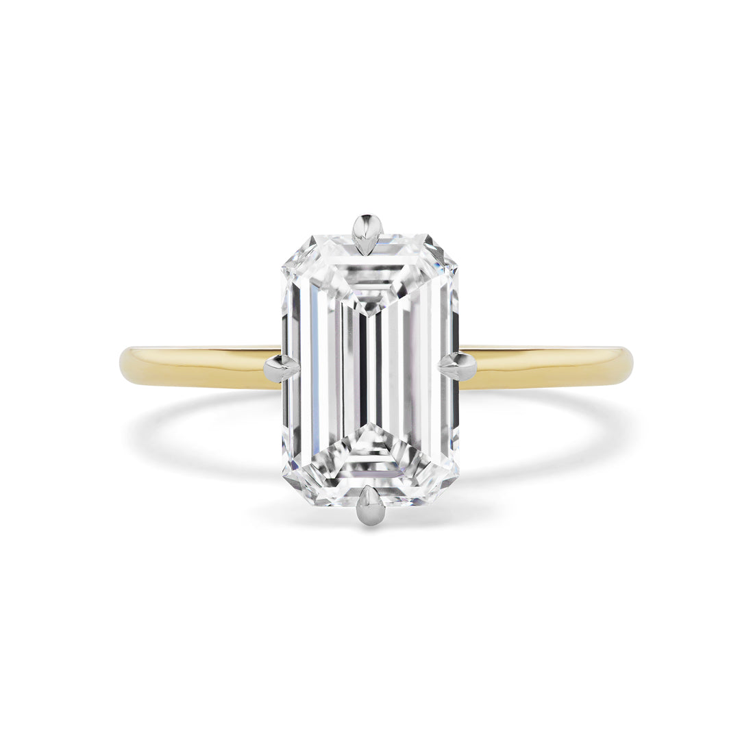 The Emerald Cut Diamond Engagement Ring with Compass Prongs showcases a large emerald-cut diamond in a solitaire setting on a thin gold band, viewed from above against a white background.