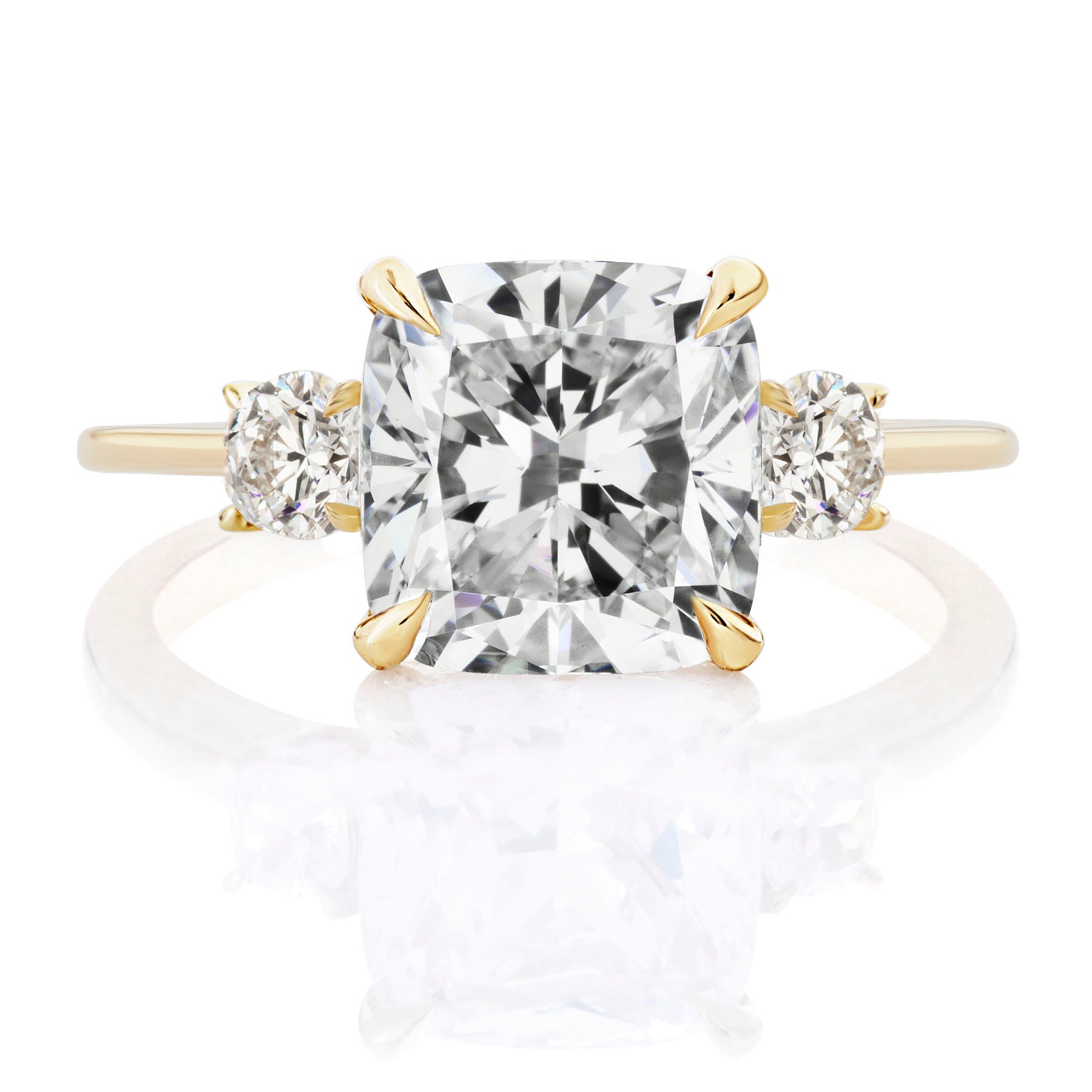 The Cushion Cut Diamond Engagement Ring with Round Side Stones showcases a gold band with a large cushion-cut center diamond and two round side diamonds, beautifully displayed against a white background.