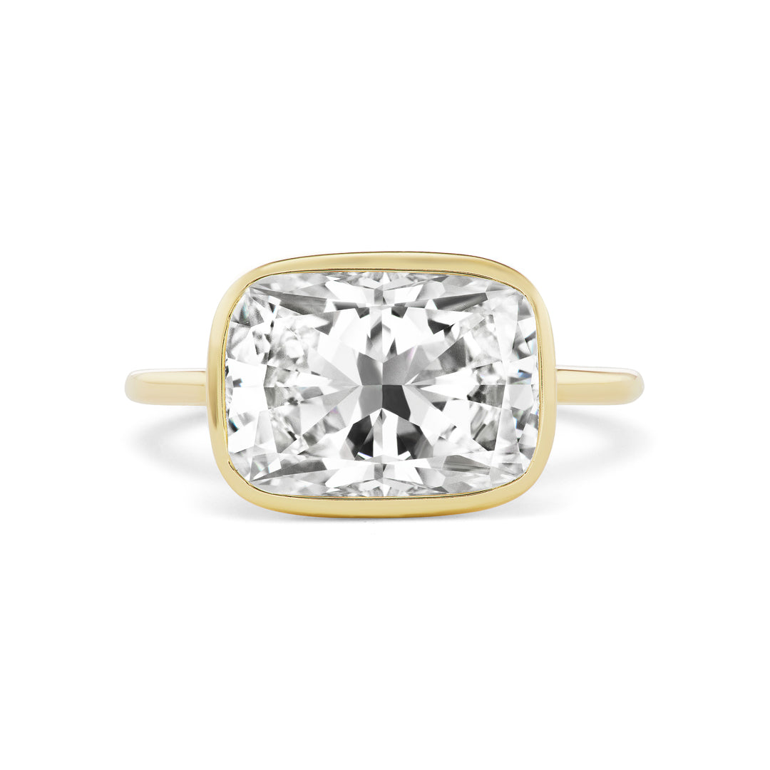 The East-West Bezel Set Cushion Cut Diamond Engagement Ring features a large cushion-cut diamond in a simple bezel setting, displayed against a white background.