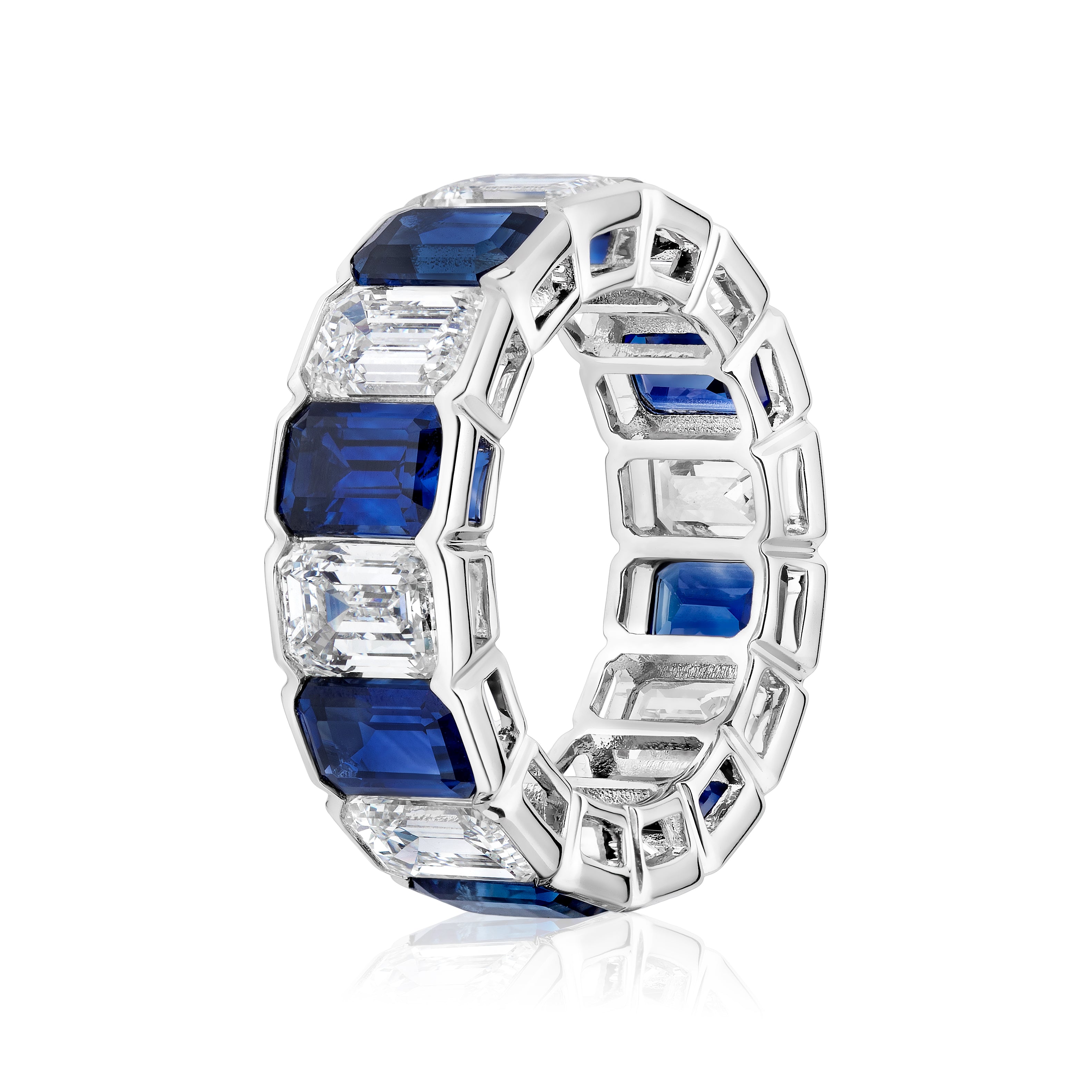 The Alternating Half-Bezel Emerald Cut Diamond and Sapphire Eternity Band is a platinum ring featuring alternating emerald-cut blue sapphires and white diamonds in a geometric design.