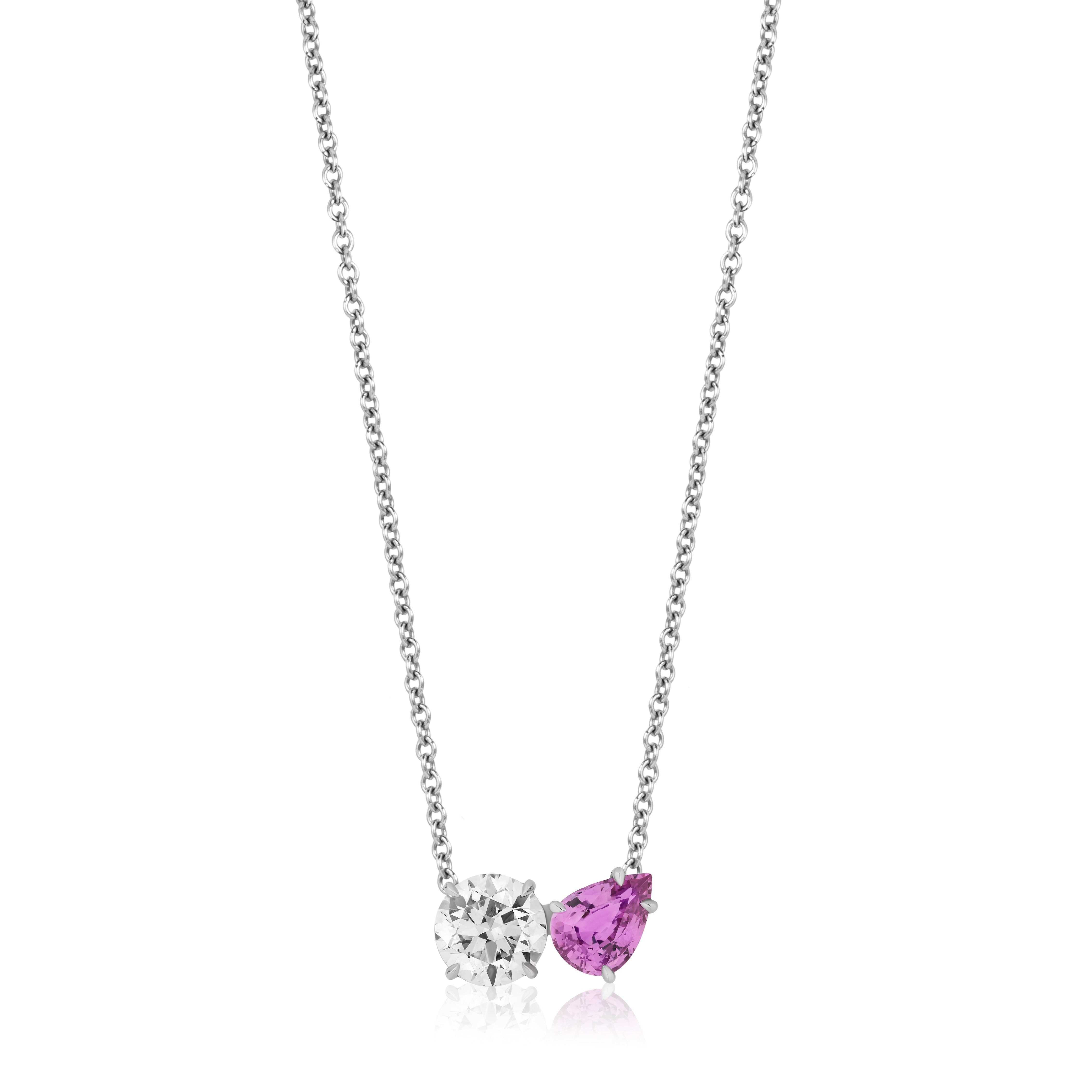 The Round Diamond and Pear Shape Pink Sapphire Toi Et Moi Pendant in White Gold is a delicate necklace with two side-by-side pendants: a round diamond and a pear-shaped pink sapphire.