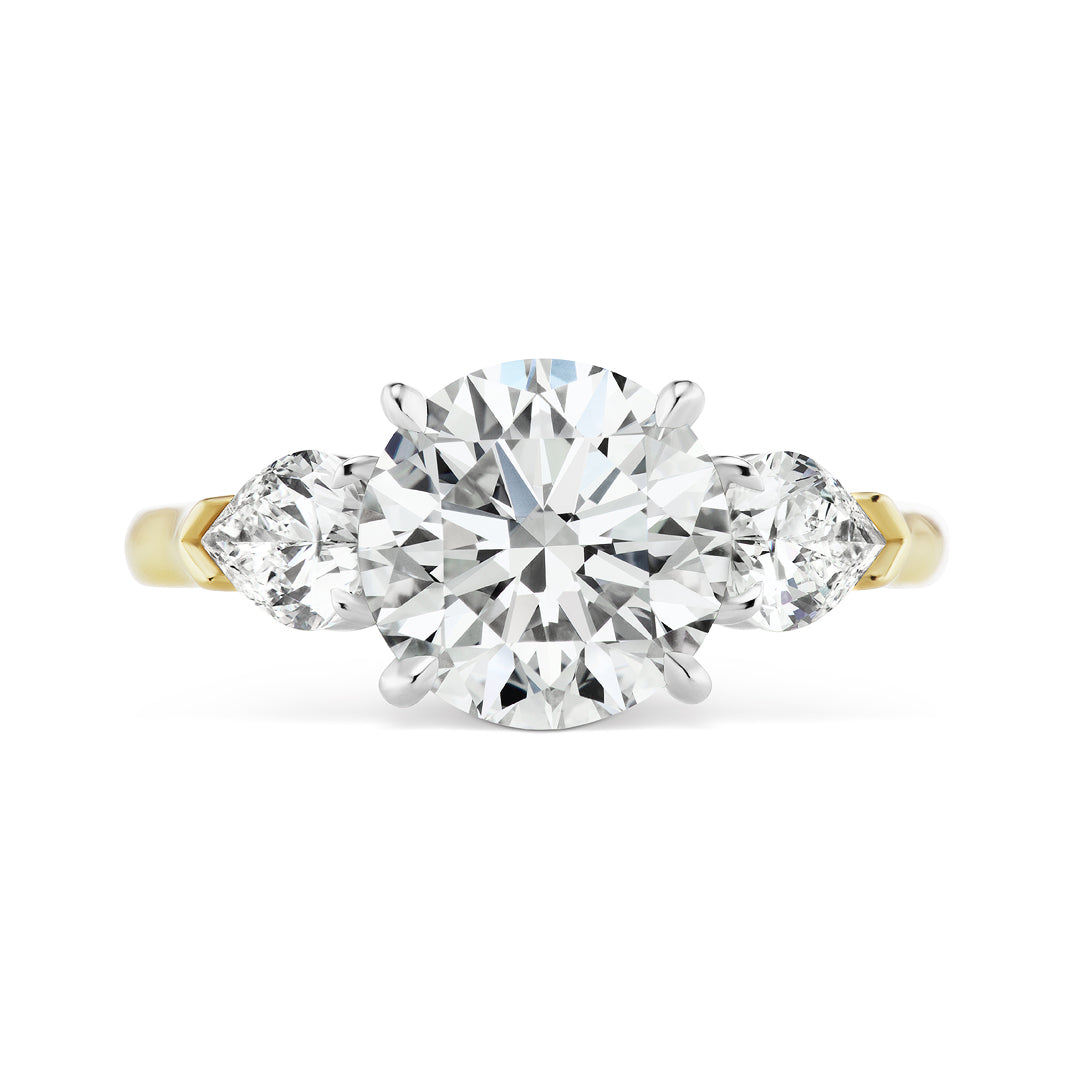 The Round Brilliant Diamond Engagement Ring with Heart Side Stones features a large round center diamond and two heart-shaped side diamonds, displayed against a white background.