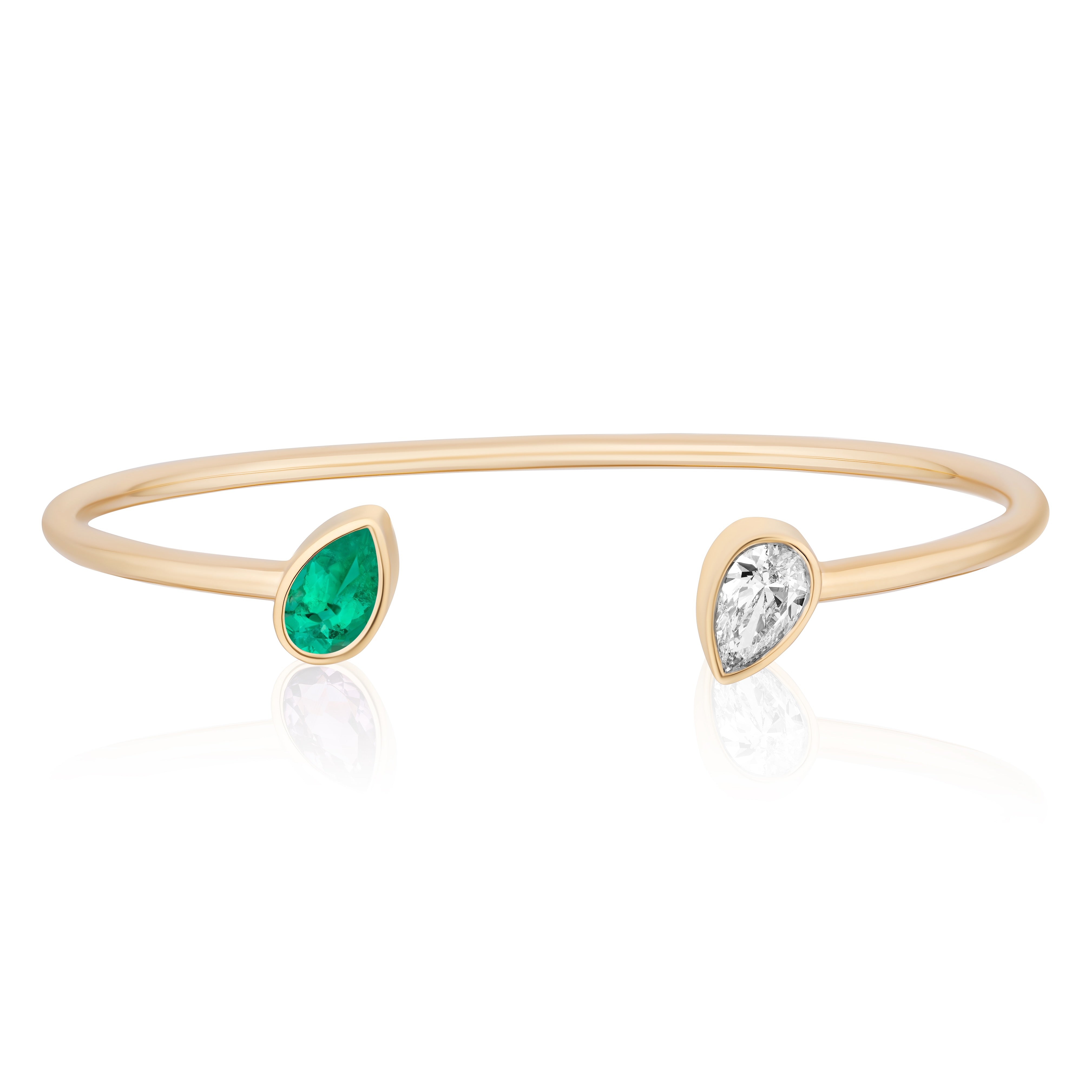 The Open Space Bangle in yellow gold features a bezel set pear shape emerald on one end and a diamond on the other, creating an elegant and modern bracelet look.