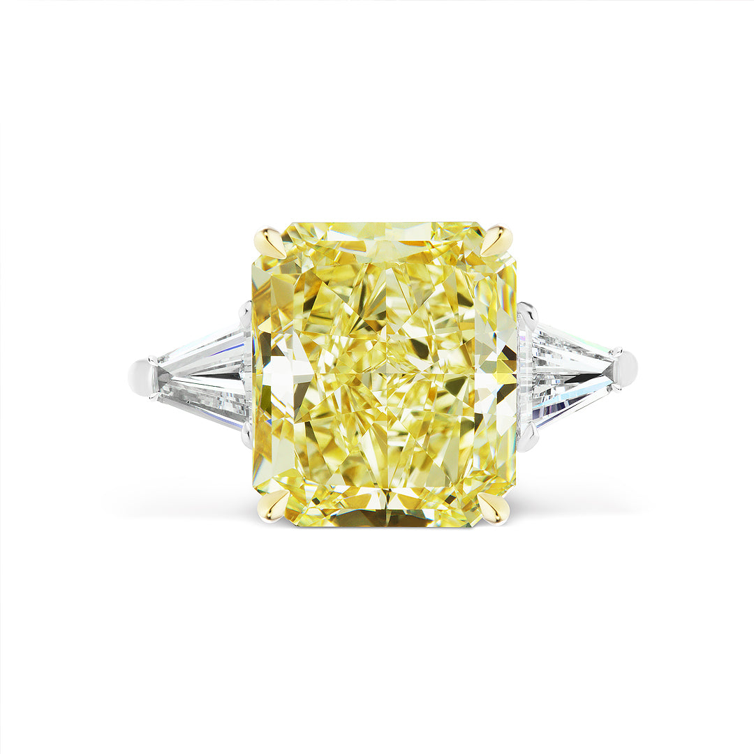 A Fancy Yellow Radiant Cut Diamond Engagement Ring features a radiant yellow diamond and tapered baguette side stones on a white band, shown against a plain white background.