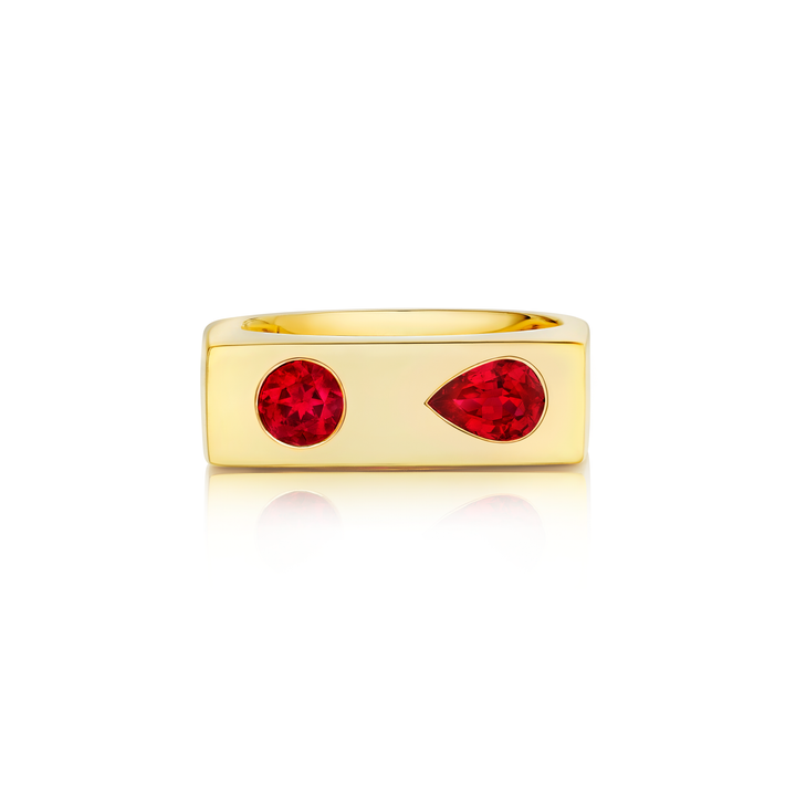 The Bar Ring with Round and Pear Cut Rubies in Yellow Gold displays two ruby gemstones, one round and one teardrop-shaped, set side by side on a yellow gold band, photographed against a white background.