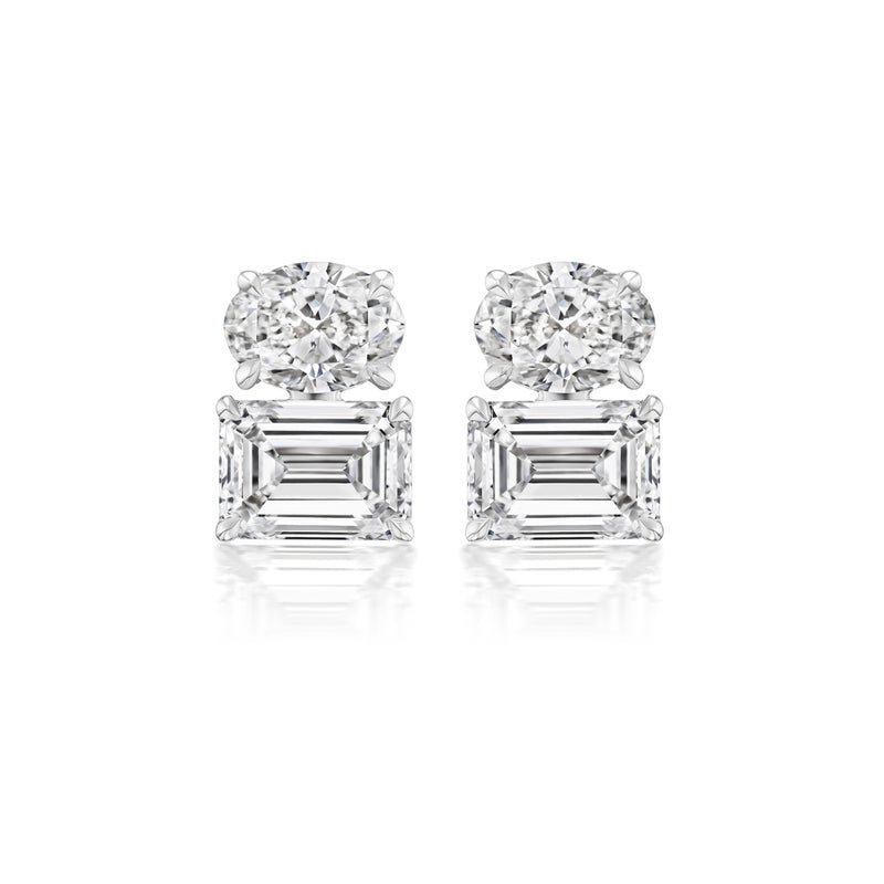 The East-West Set Oval and Emerald Cut Diamond Studs in White Gold feature an oval diamond above a larger emerald cut diamond, set in 18k white gold against a white background.