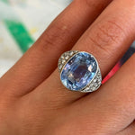 A close-up of a hand wearing the 1930s Sapphire and Diamond Ring, featuring a large oval light blue Ceylon sapphire at its center, flanked by small clear rose-cut diamonds on either side.