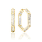 The Chrysler Hoops with Baguette Diamonds are octagonal 18K gold earrings set with vertical white baguette diamonds, shown against a white background. One earring stands upright while the other is partly open, showcasing their elegant thickness.