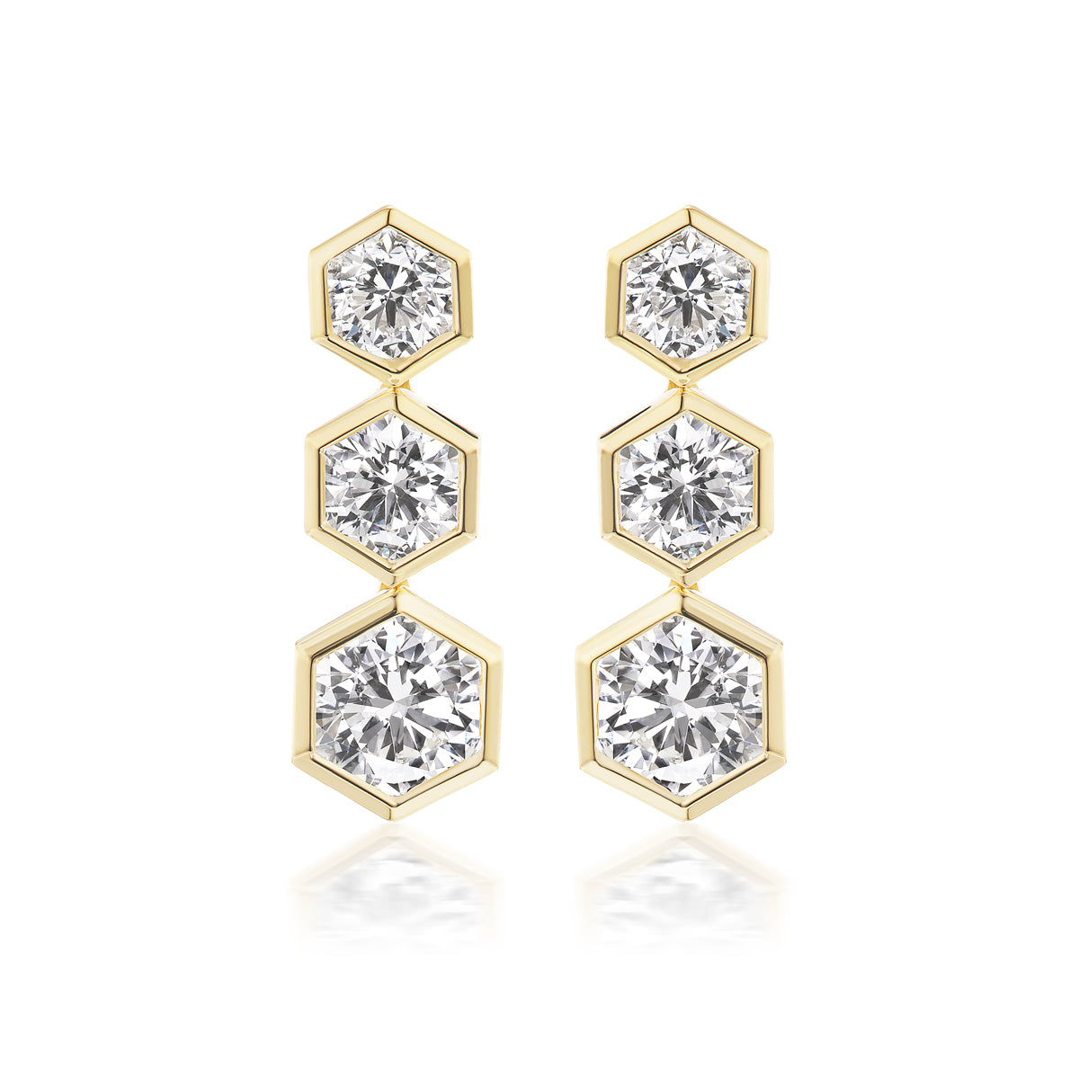 The Graduated Hexagon Bezel Set Drop Earrings feature 18K yellow gold with three vertically arranged round brilliant diamonds in hexagonal bezels, each stone increasing in size from top to bottom.
