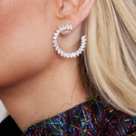 Close-up of a person wearing Jumbo Climbing Ivy Hoops in white gold with marquise diamonds, SI1-SI2 clarity. The person has long blonde hair and a black top with colorful metallic threads.