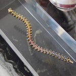 The Chroma Marching Alternating Bezel Set Marquise Sapphire Tennis Bracelet in yellow gold is displayed on a clear rectangular tray, with other jewelry pieces visible in the background.