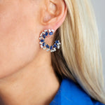 Close-up of a woman with long blonde hair in a vibrant blue shirt wearing Chroma Empire Alternating Sapphire and Diamond Front-to-Back Earrings. The neutral background highlights the sparkling blue sapphires and diamonds in her jewelry.