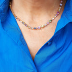 A person wearing a vibrant blue shirt and the Chroma Kaleidoscope Mixed Shape Sapphire and Diamond Tennis Necklace in Yellow Gold. The photo is cropped to show the neck, collar, and upper chest.