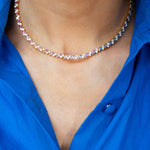 A close-up of a person wearing the Chroma Match Point Multicolor Tennis Necklace in yellow gold with marquise sapphires and round diamonds, paired with a vibrant blue button-up shirt—an eye-catching fine jewelry piece.