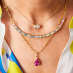 A close-up of a person wearing the Ombré Smile Bar Necklace in yellow gold with Asscher cut diamonds and multicolor sapphires, styled with layered gold chains and a colorful patterned shirt.