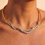 A close-up of a woman's neck wearing the Coil Graduated Round Diamond and Omega Chain Necklace in yellow gold and platinum, featuring a wavy design with sparkling round diamonds along the front.