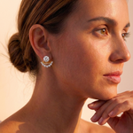 A woman with brown hair in a low bun wears Coil Draped Diamond Ear Jackets in yellow gold and platinum, featuring a large stud and curved row of natural diamonds, as she gazes to the side with her hand near her chin in warm light.