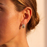 Close-up of a woman’s ear wearing Coil Hoops with Graduated Round Diamond Borders in Yellow Gold and Platinum. Her hair is pulled back, and warm light highlights the diamonds' sparkle against her skin.