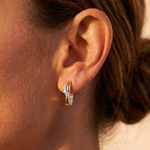 Close-up of a woman with light skin and brown hair pulled back, wearing Coil Graduated Round Diamond Wave Huggies in yellow gold and platinum.
