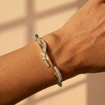 A close-up of a wrist wearing the Coil Wave Diamond Bangle in Yellow Gold and Platinum, featuring wavy rows of sparkling natural diamonds against a softly lit background with gentle shadows.