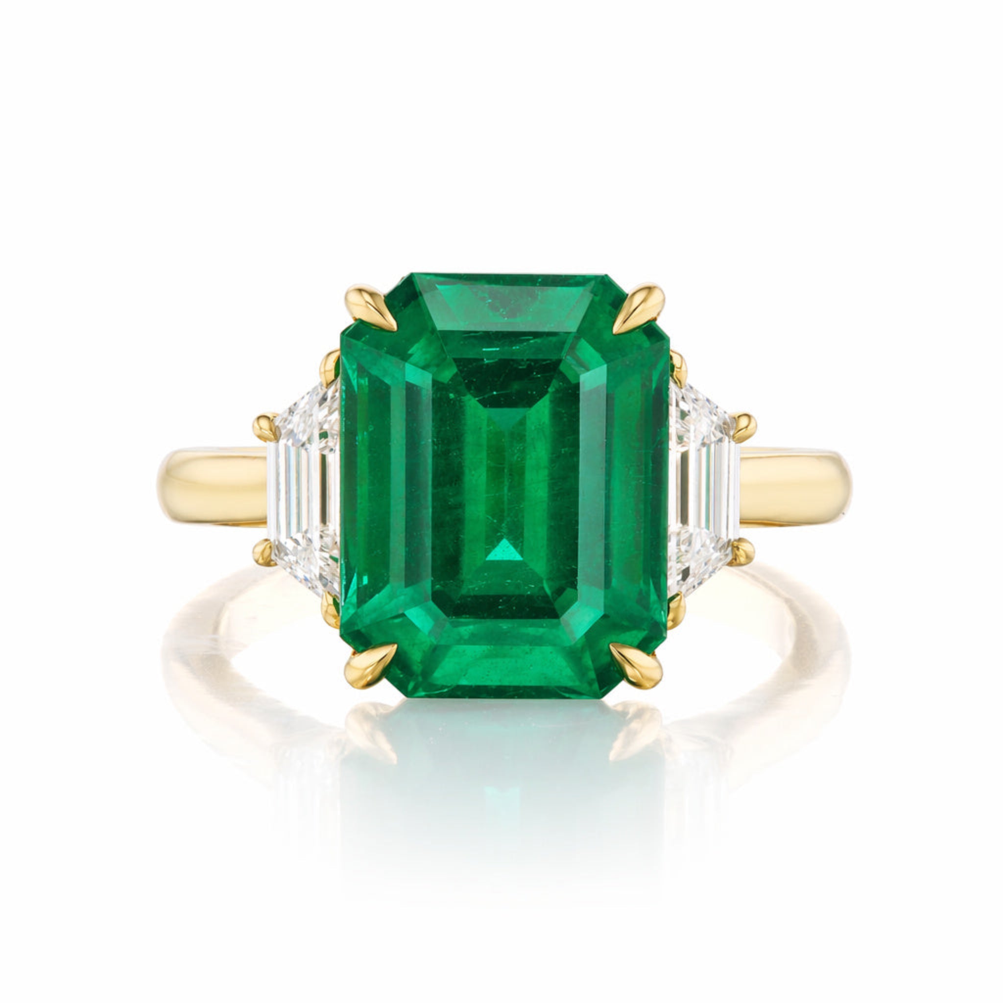 An Emerald Cut Emerald Engagement Ring in Yellow Gold with trapezoid baguette diamond side stones is displayed on a white background.