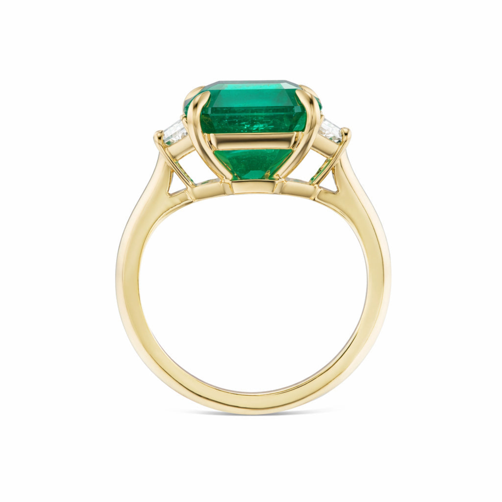 Emerald Cut Emerald Engagement Ring in Yellow Gold features a large rectangular green emerald at the center, flanked by two trapezoid baguette diamond side stones, with a detailed setting visible from the side.
