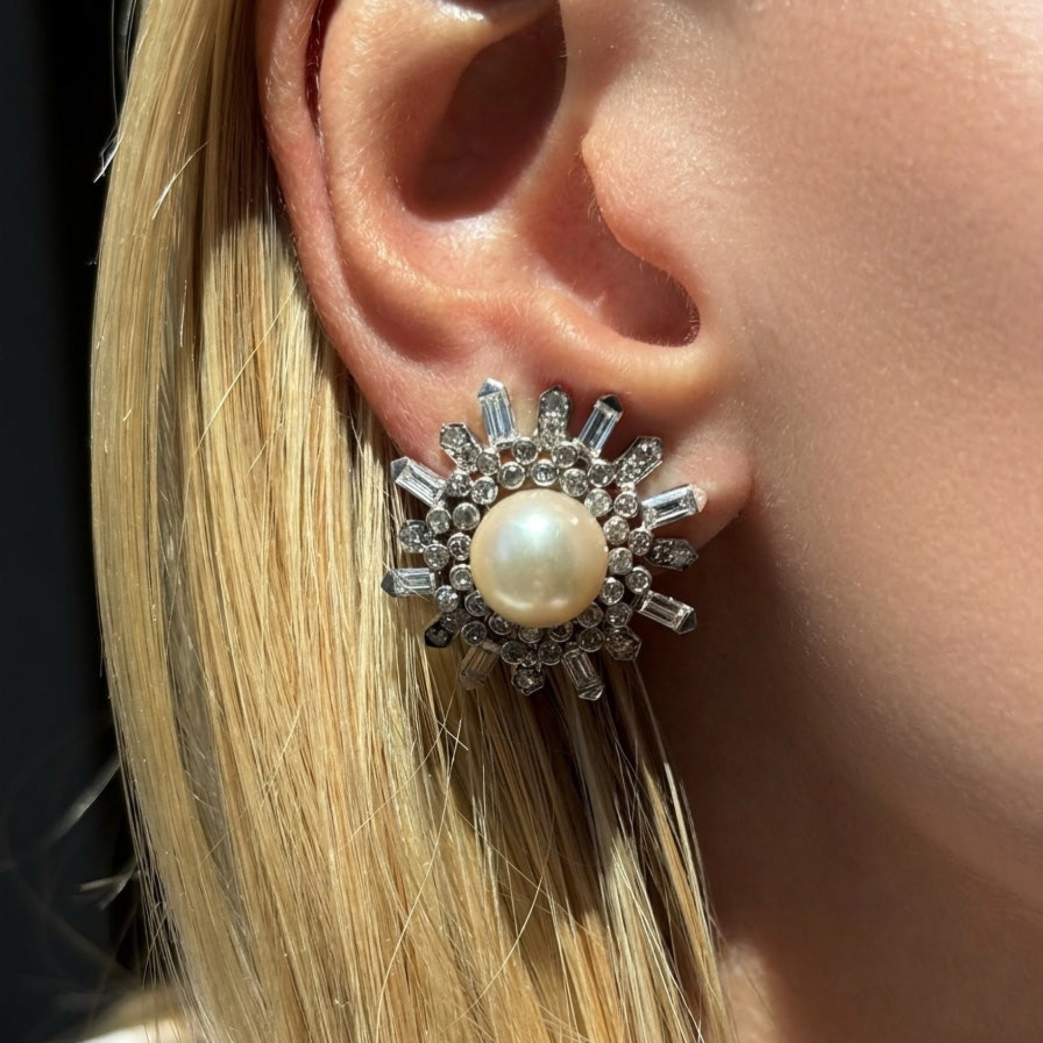 A close-up of a woman’s ear showcases the Van Cleef & Arpels Pair of Pearl and Diamond Earclips, inspired by vintage 1960s elegance. Blonde hair and sunlight highlight their large, intricate design—a refined tribute to timeless craftsmanship.