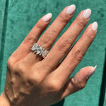 A hand with light pink manicured nails wears a stacked Diamond Band Ring on the ring finger, set against a green textured background.