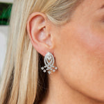 Close-up of a woman's ear adorned with a Pair of Diamond Earrings, circa 1930s, featuring large, intricately layered silver design embellished with small star-shaped accents. Her blonde hair is tucked behind her ear to highlight the detailed jewelry, which evokes the elegance of antique platinum pieces from the era.