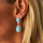 A close-up of a blonde woman wearing the Pair of Turquoise and Diamond Earclips, featuring two oval turquoise cabochons set in 14K white gold, each surrounded by a halo of sparkling diamonds.