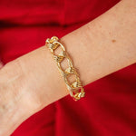 A close-up of a wrist adorned with the Van Cleef & Arpels Reeded Gold Link Bracelet in 18K gold, featuring chunky twisted links, set against a vivid red fabric background.