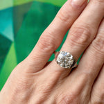 A close-up of a hand wearing the Platinum and Diamond Ring, featuring a 4.17 carat old European-cut diamond set in platinum, against a green geometric-patterned background.