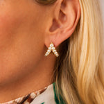 Close-up of a woman's ear wearing Vintage Bulgari Gold and Diamond Earclips, featuring a stunning chevron V-shaped design crafted in 18K yellow gold and accented with clear gemstones. The woman has blonde hair and is dressed in a floral-patterned top, capturing an elegant look inspired by Bulgari's iconic style.