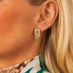 A close-up of a woman's ear wearing a Vintage Bulgari Gold "Parentesi" Earclip, crafted in 18K yellow gold with an engraved geometric pattern that echoes Bulgari's iconic style. Part of her blonde hair and a patterned collar are also visible.